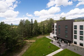 A modern building with multiple floors, a courtyard with seating, and a surrounding forested area.