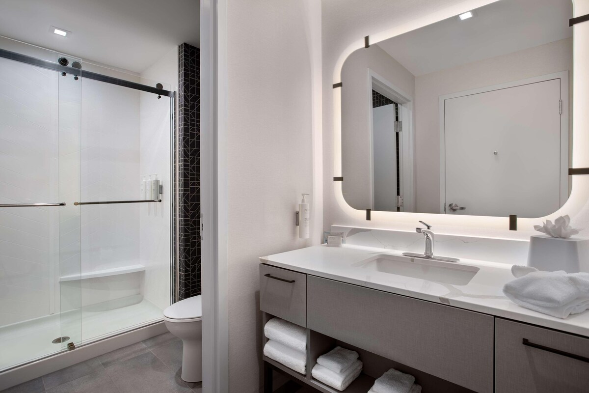 A modern bathroom with a glass-enclosed shower, a large mirror, and a white vanity with a sink.