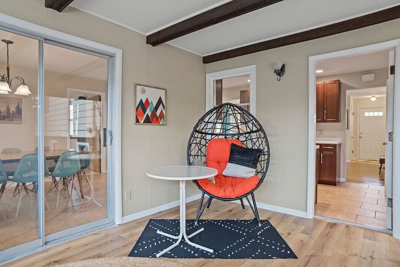 A modern interior with a glass door leading to a dining area, a round hanging chair with cushions, and a small table.