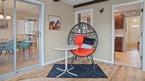 Un interior moderno con una puerta de cristal que da a un comedor, un sillón colgante redondo con cojines y una pequeña mesa.