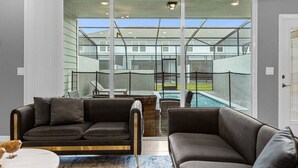 A modern living room with a sectional sofa, a coffee table, and a view of a swimming pool through large glass doors.