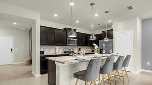 A modern kitchen with dark cabinets, a large island with bar stools, stainless steel appliances, and pendant lighting.
