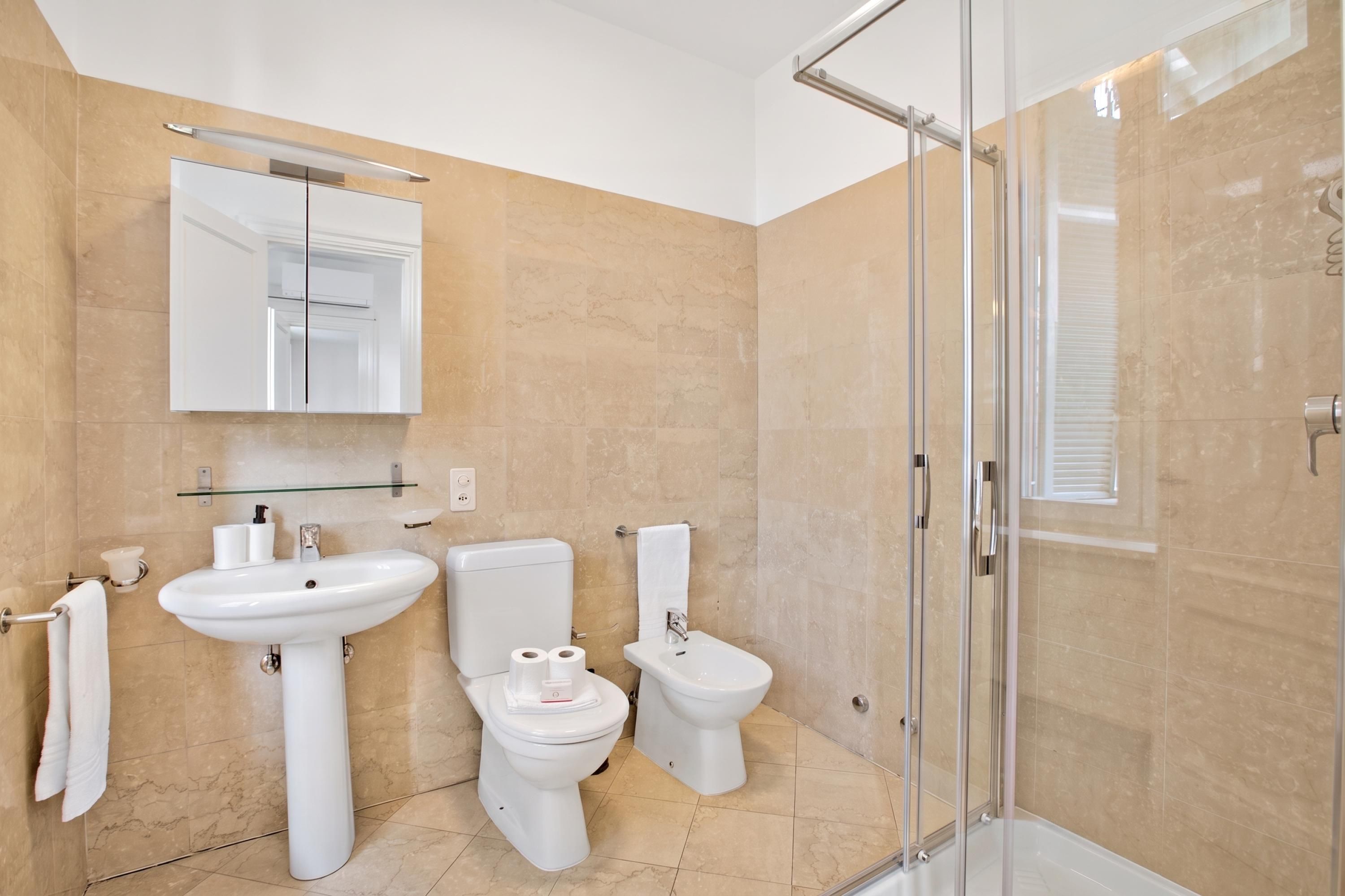 A modern bathroom with a glass shower enclosure, a large mirror, and two toilets.