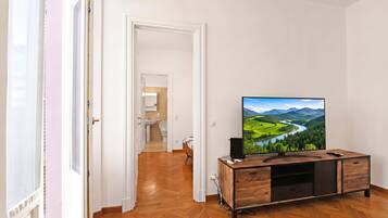 A hotel room with a wooden floor, a TV on a wooden stand, and a view of a landscape through the window.