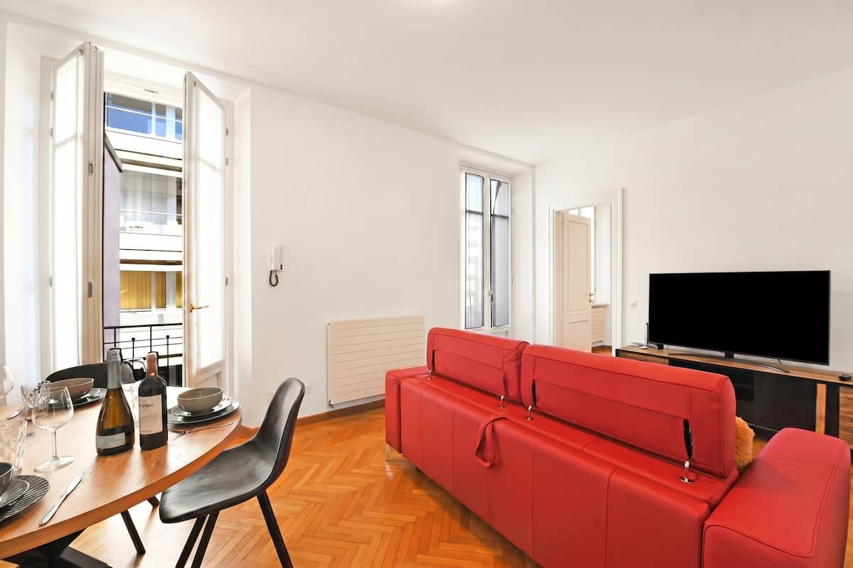 Una sala de estar moderna con comedor, un sofá rojo, un televisor de pantalla plana y un balcón con baranda.