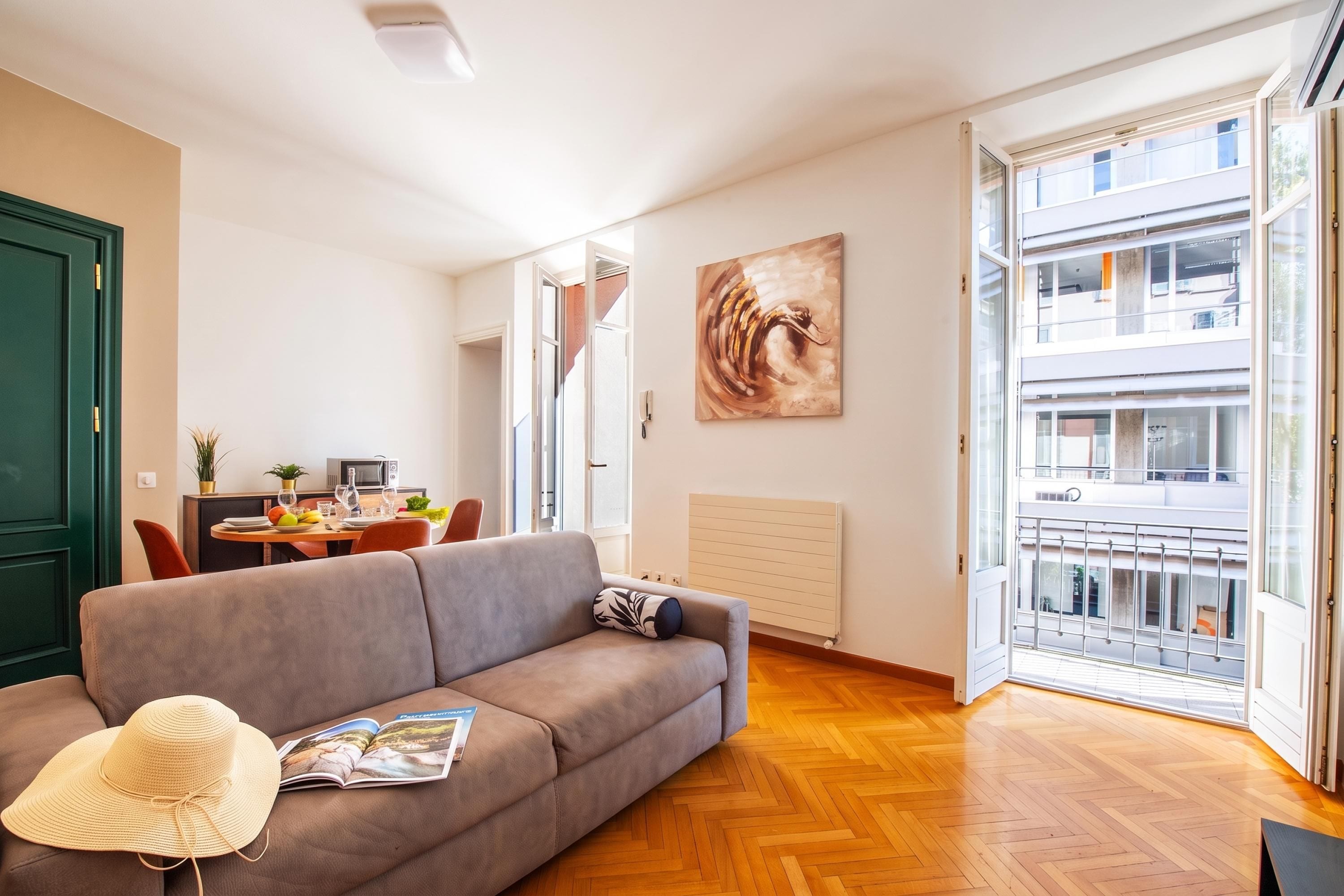 A modern living room with a sofa, a dining area, and a view of the city through large windows.
