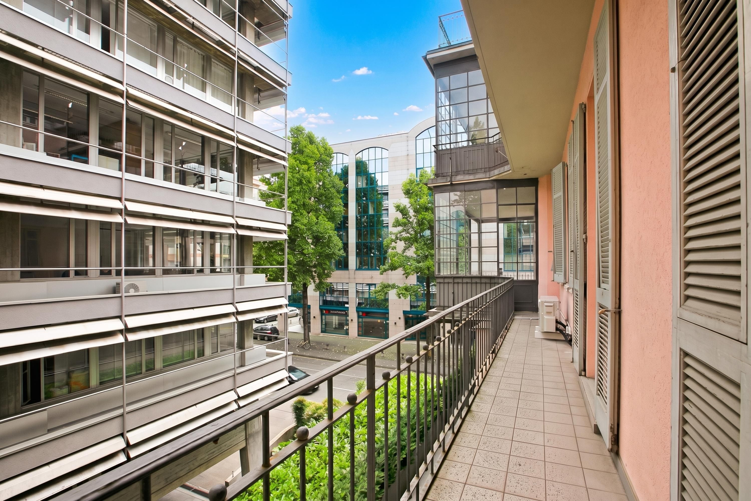 A modern building with multiple floors, large windows, and a balcony with a metal railing.