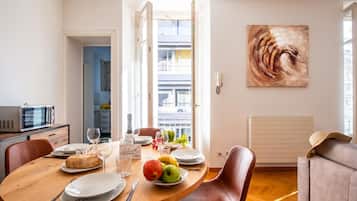 A dining area with a round table, chairs, a microwave, a painting, and a view of the outside.