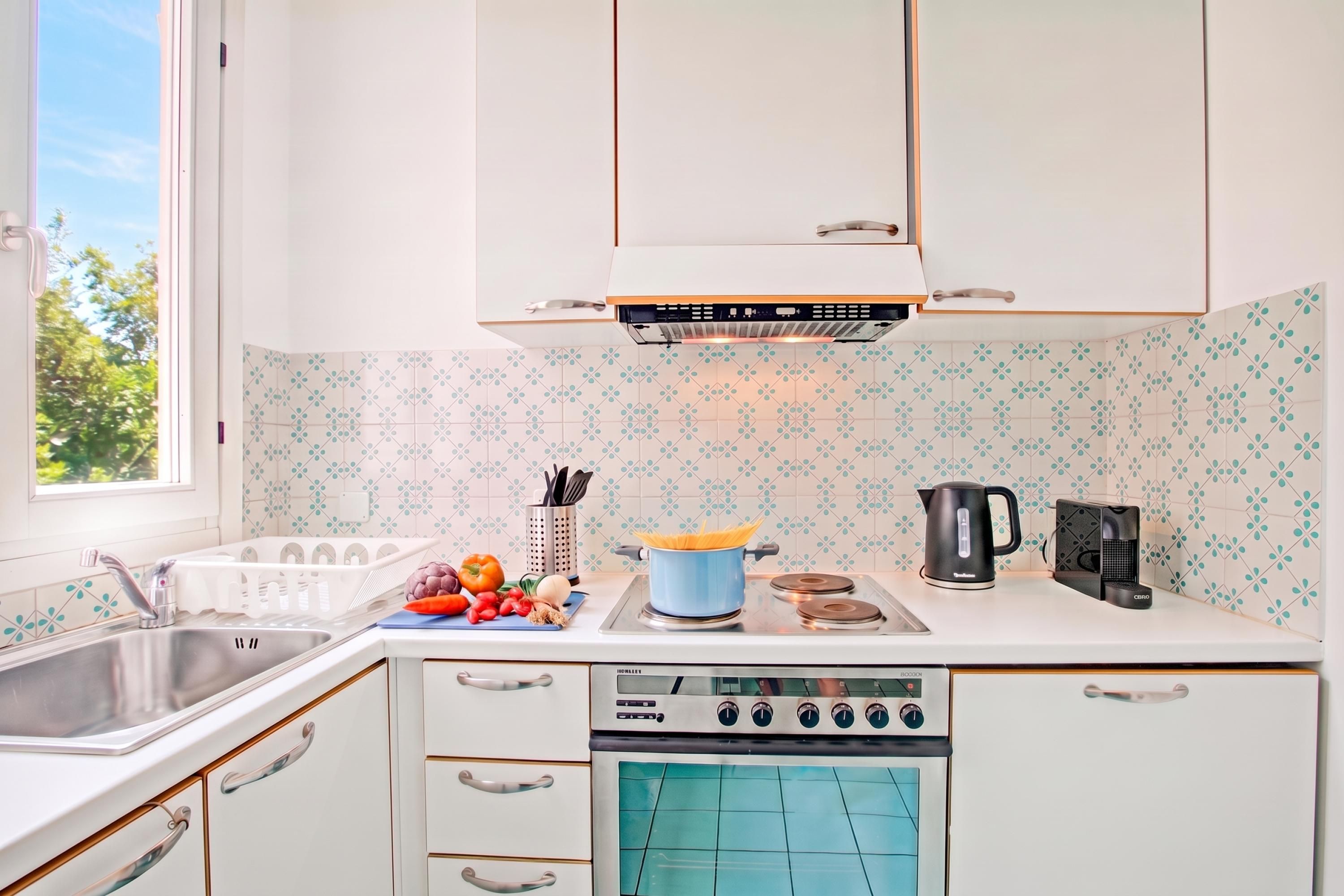 A kitchen with white cabinets, a stove, a kettle, and a sink.