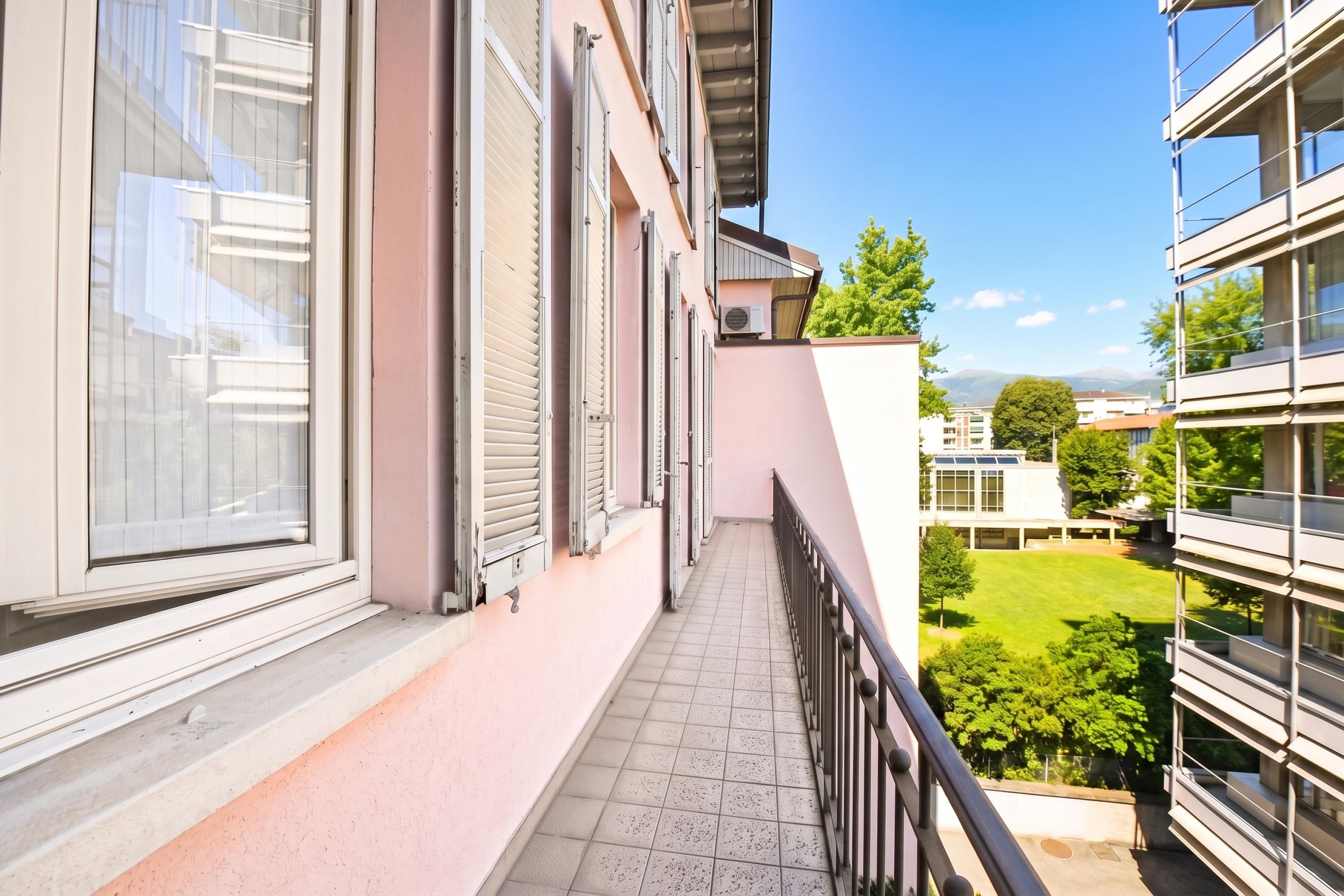 Un balcon donnant sur un parc verdoyant et des immeubles.