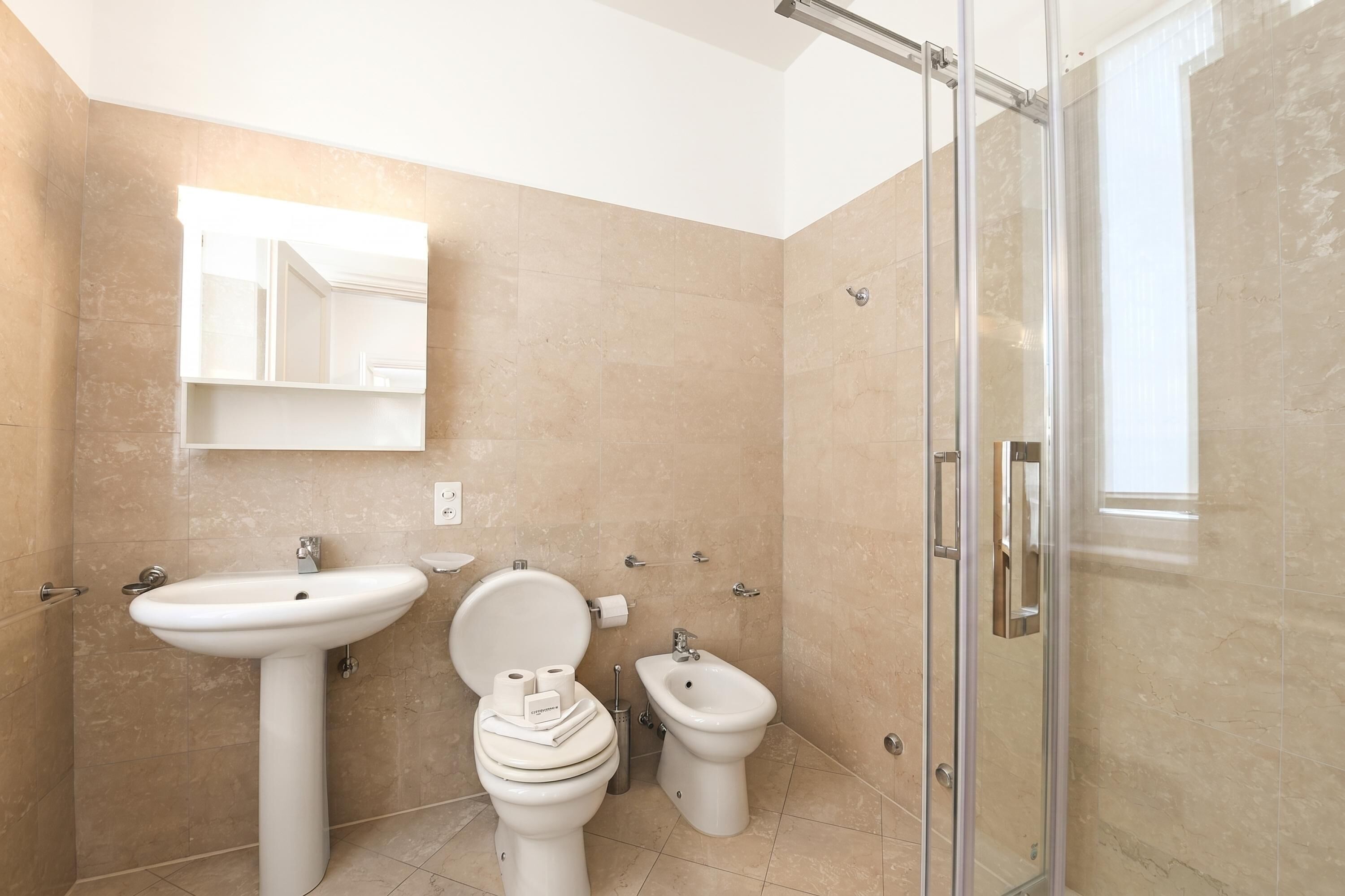 A bathroom with a sink, toilet, bidet, and a glass shower enclosure.
