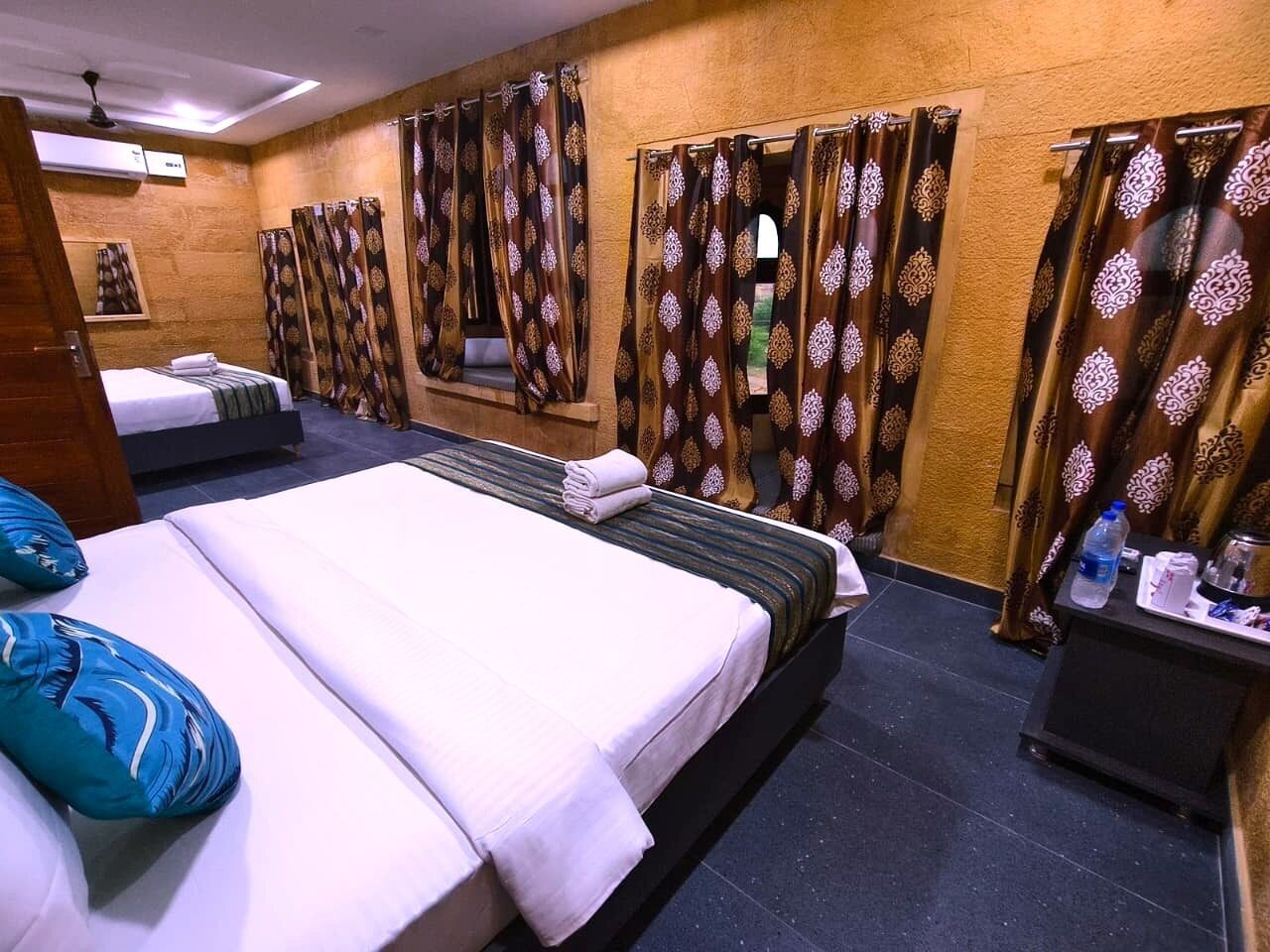 A hotel room with two beds, a small table with a water bottle, and curtains with a pattern.