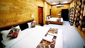 A hotel room with two beds, a wooden headboard, a ceiling fan, and a wall with patterned curtains. - Hotel Jodhani Regency (Jaisalmer)