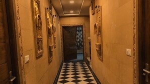 A hallway with a black and white checkered floor, ornate wall decorations, and a door at the end. - Hotel Jodhani Regency (Jaisalmer)