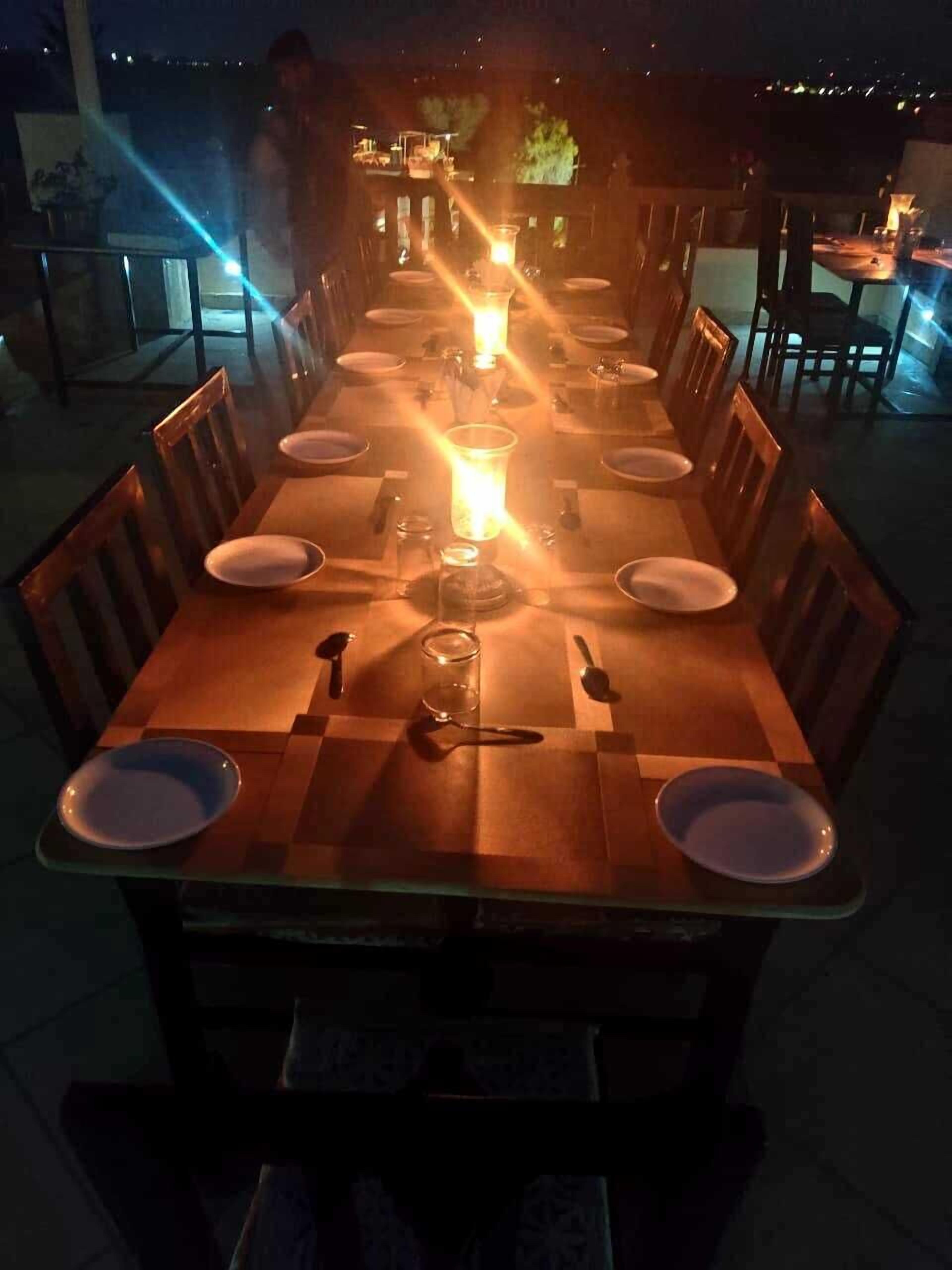 A long dining table with chairs, lit by a central candle, set for a meal.