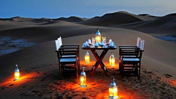 A desert table set with chairs and lanterns, surrounded by sand dunes. - Hotel Jodhani Regency (Jaisalmer)