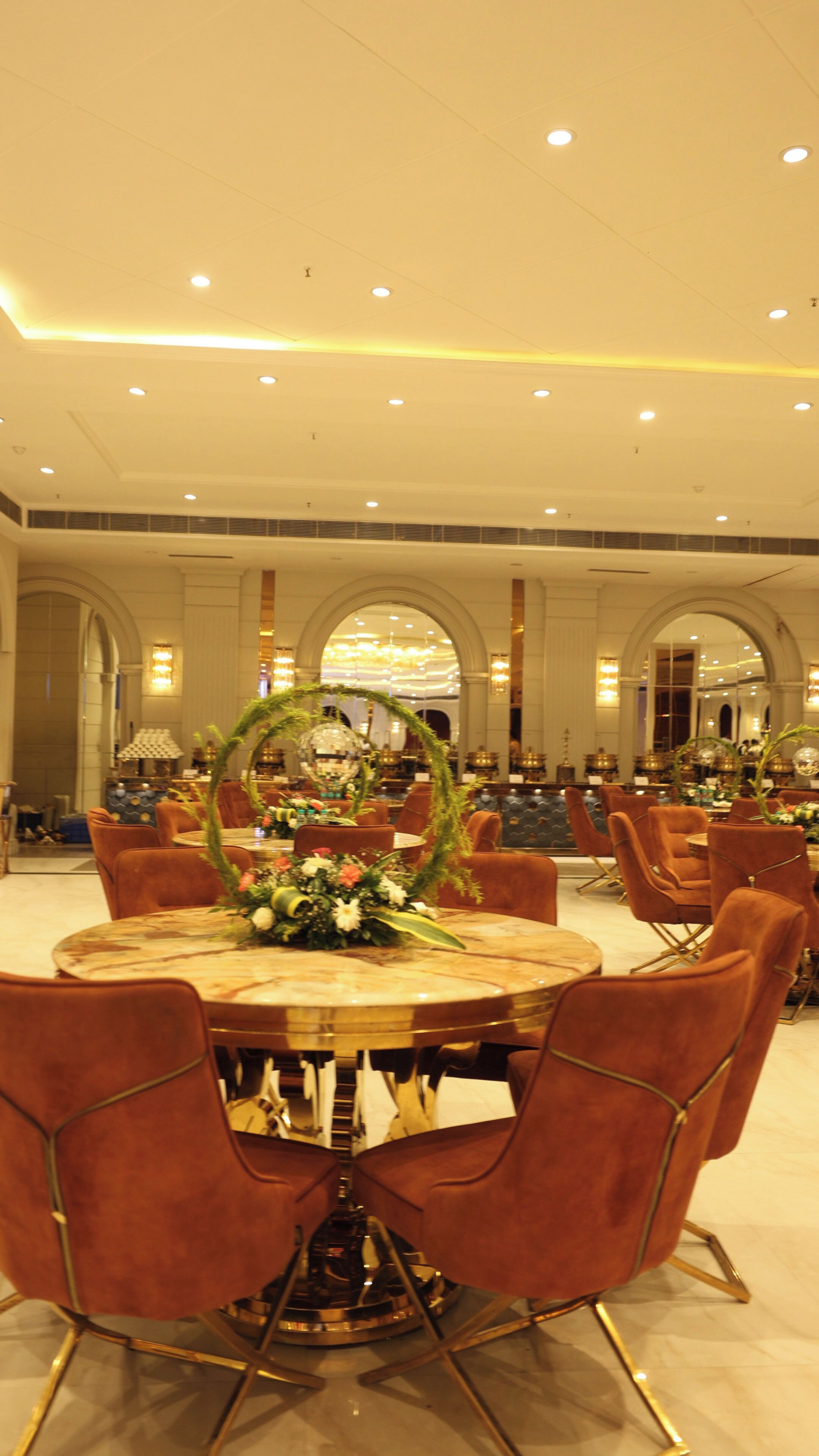 A dining area with round tables, red upholstered chairs, and a central floral arrangement.