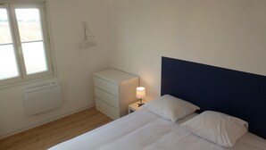 Ein Schlafzimmer mit Bett, Nachttisch, Lampe und Fenster.