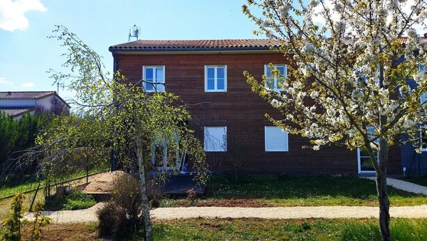 Ein zweistöckiges Backsteingebäude mit zahlreichen Fenstern und einem kleinen Garten mit Bäumen und einem Kiesweg.
