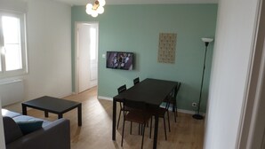 Ein Wohnzimmer mit einer Couch, einem Couchtisch, einem Esstisch mit Stühlen, einem an der Wand befestigten Fernseher und einer Stehlampe.