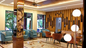 A modern lobby with marble flooring, blue seating, a ceiling fan, and a large mirror. -  Woods Inn Resort (Airport Hotel) (Bhopal)