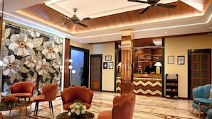 A lobby with a reception desk, plush seating, a ceiling fan, and a decorative wall. -  Woods Inn Resort (Airport Hotel) (Bhopal)