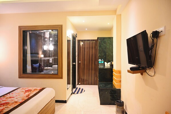 A hotel room with a bed, a television mounted on the wall, a window with a view of the outside, and a door leading to the bathroom.