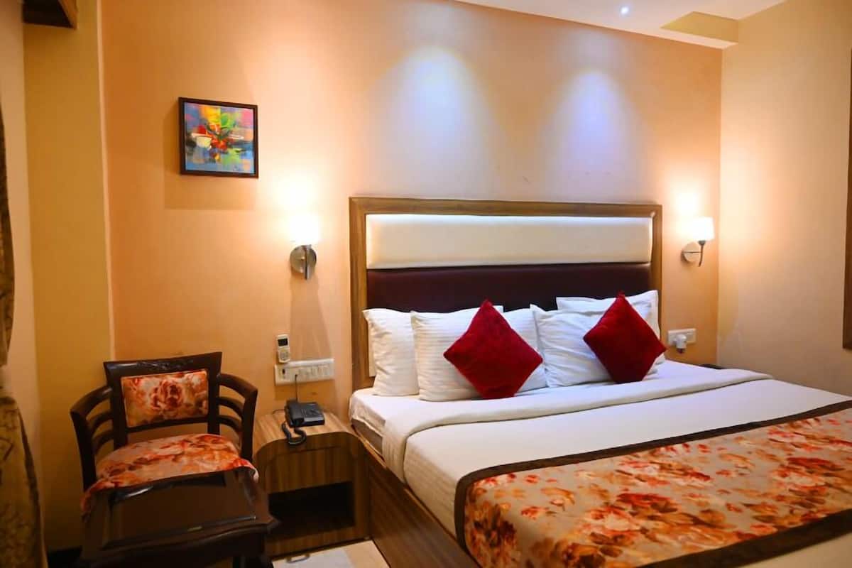 A hotel room with a bed, a chair, a nightstand, a telephone, and a painting on the wall.