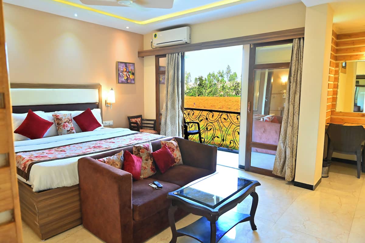 A hotel room with a bed, a sofa, a glass table, and a balcony with a view of greenery.