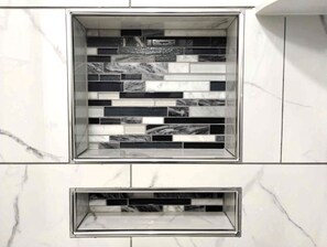 A bathroom with a tiled backsplash featuring a mix of black, white, and gray tiles. Below the backsplash, there is a rectangular sink with a chrome finish.