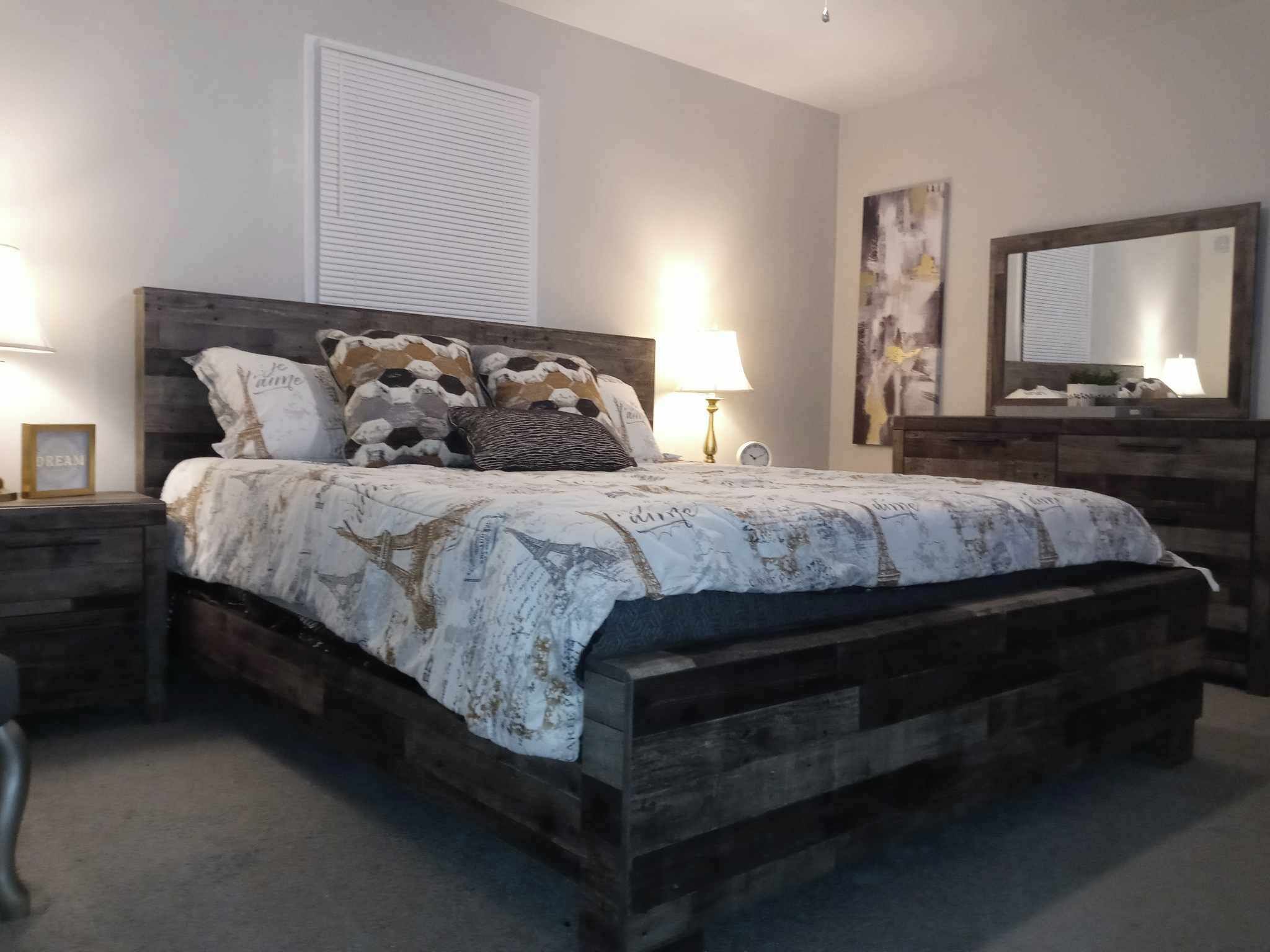 A bedroom with a wooden bed, a nightstand with a lamp, a dresser, and a mirror.