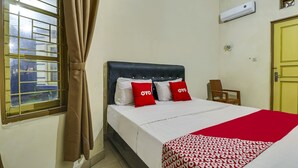 Una habitació d'hotel amb un llit, una finestra amb cortines, aire condicionat i una porta.