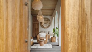 A wooden door leading into a room with a wicker chair, a round mirror, and a potted plant. - Villa Madissa by Villa Finder (Canggu)