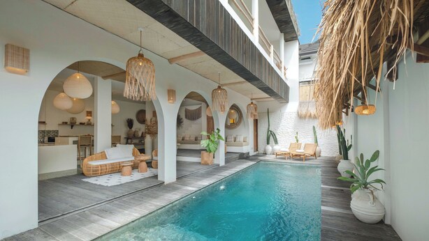 A poolside area with a clear pool, lounge chairs, and a dining area with a kitchen in the background. - Villa Madissa by Villa Finder (Canggu)