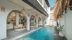 Un espace aménagé au bord de la piscine, avec une piscine à eau claire, des chaises longues et un coin repas doté d’une cuisine en arrière-plan.