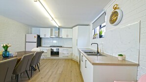 Une cuisine moderne avec des meubles blancs, une table à manger en bois et une chaise rose.