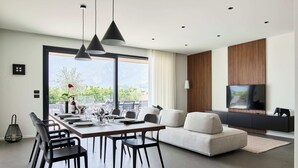 Un salon moderne comprenant un coin repas, un grand téléviseur et une vue sur la verdure environnante.