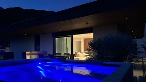 Un espace piscine extérieur moderne, doté d’un coin salon et offrant une vue sur l’intérieur.