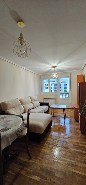 Una sala de estar con un sofá, una mesita y una silla. Se ven edificios a través de las ventanas.