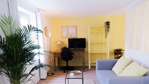 Una sala de estar con un escritorio, televisor, sofá y una planta grande en maceta.