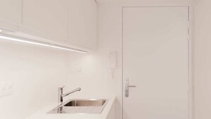 Una cocina moderna con armarios blancos, un lavamanos de acero inoxidable y una puerta con manija.
