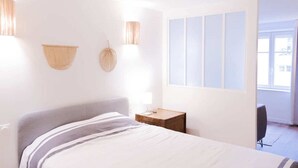 Habitación de hotel con cama, lámparas de noche, mesita de noche de madera y vistas al exterior a través de una ventana.