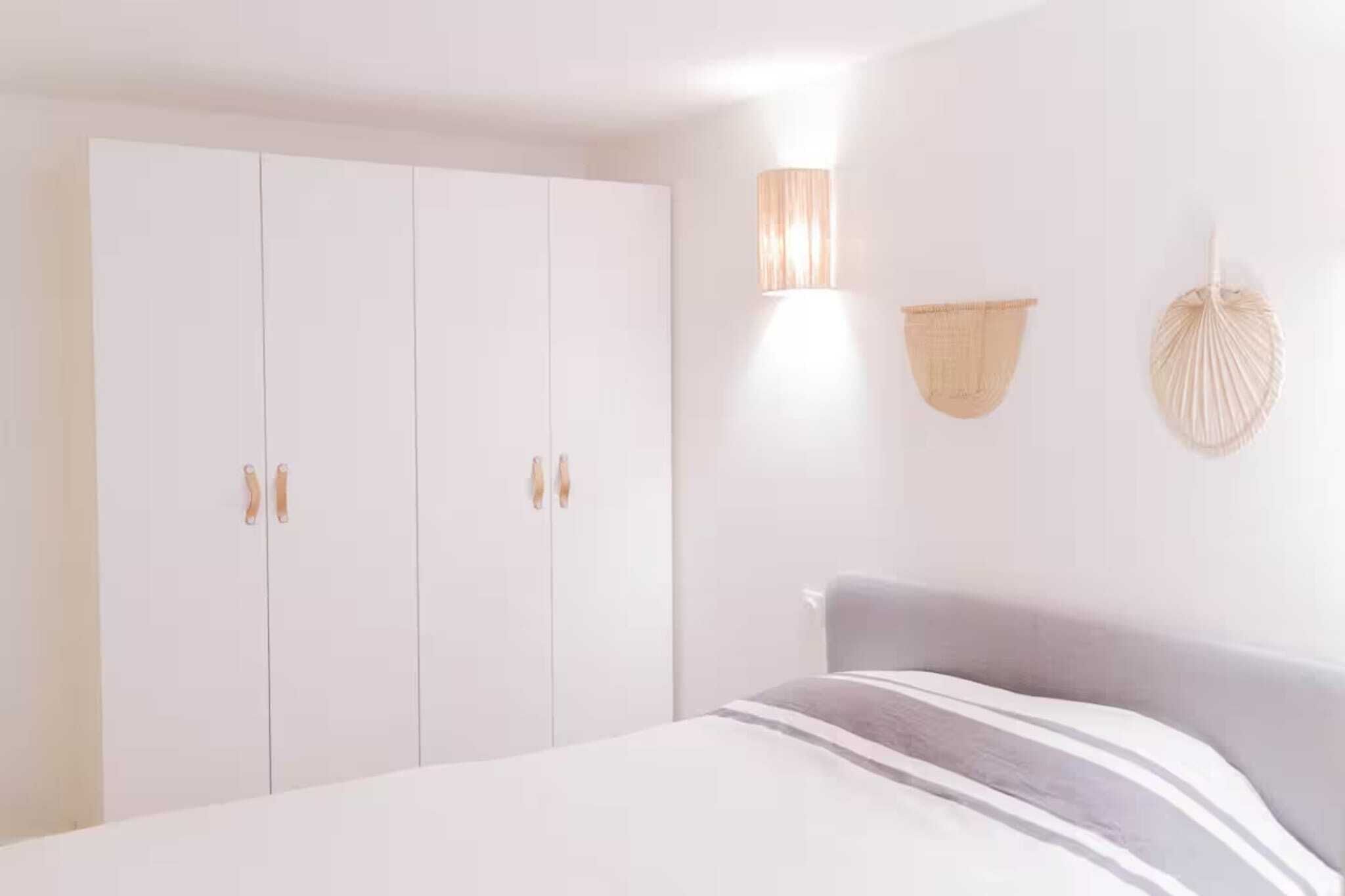 A bedroom with a bed, a wardrobe, and a wall-mounted lamp.