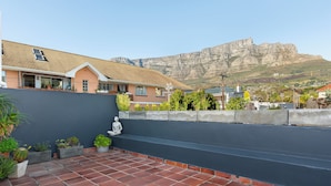 A rooftop terrace with red tiles, a grey wall, and a view of a mountain.