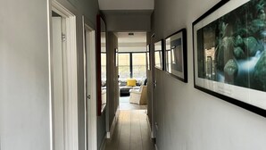 Un pasillo con un radiador, obras de arte enmarcadas en las paredes y vistas a una sala de estar con un sofá y un cojín amarillo.
