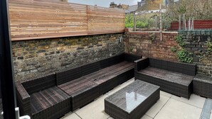 Un patio en la azotea con piso de madera, pared de piedra y mobiliario de ratán negro.