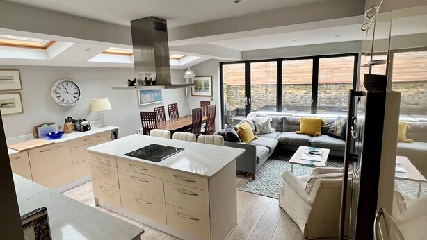 Una cocina moderna con una isla central, un área de comedor con sofá y mesa de centro, y un ventanal con vistas al exterior.