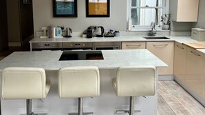 Una cocina moderna con una isla central, taburetes de bar, horno empotrado y ventana con vistas al jardín.