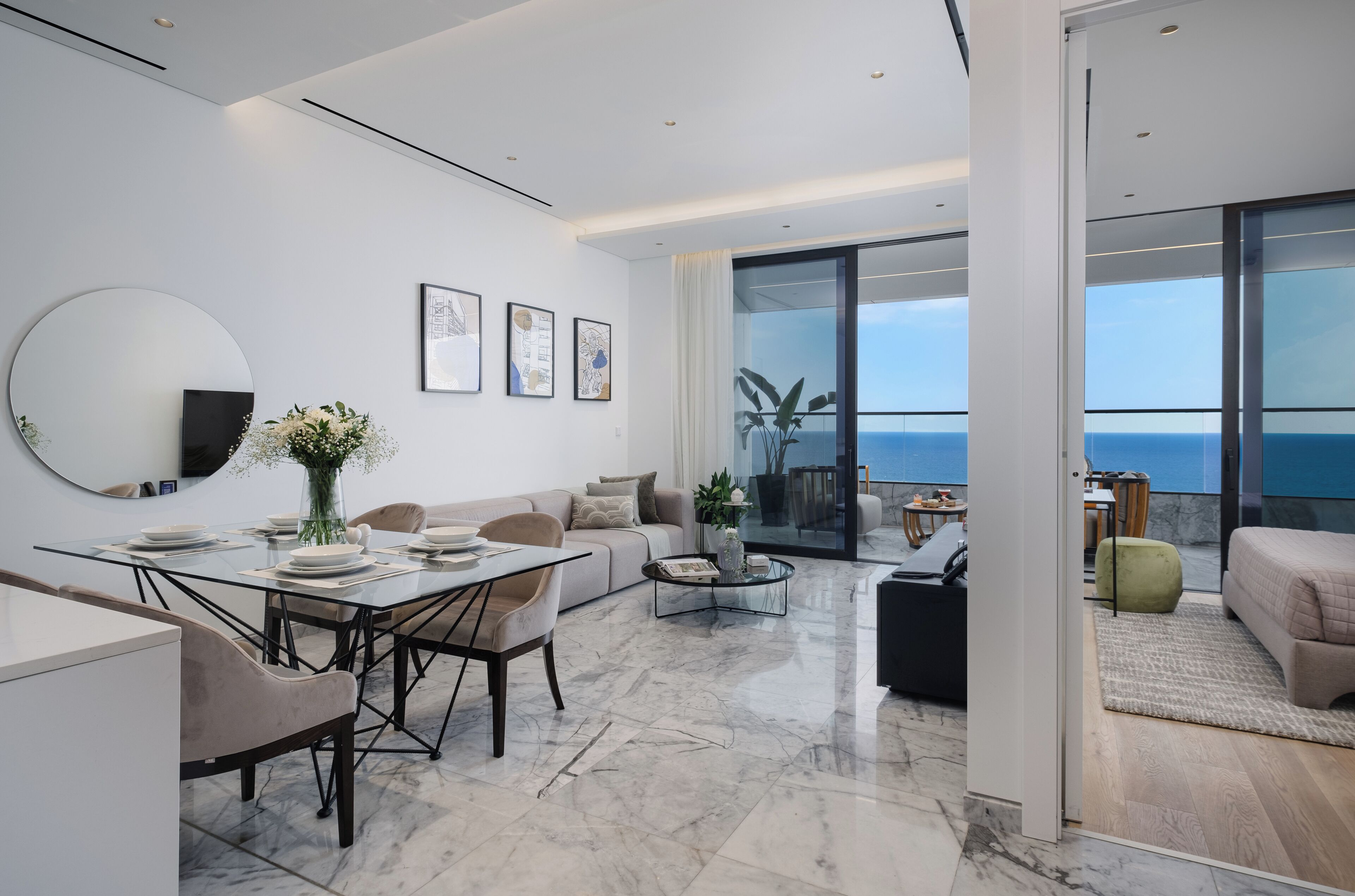 A modern living room with a dining area, large windows, and a view of the sea.