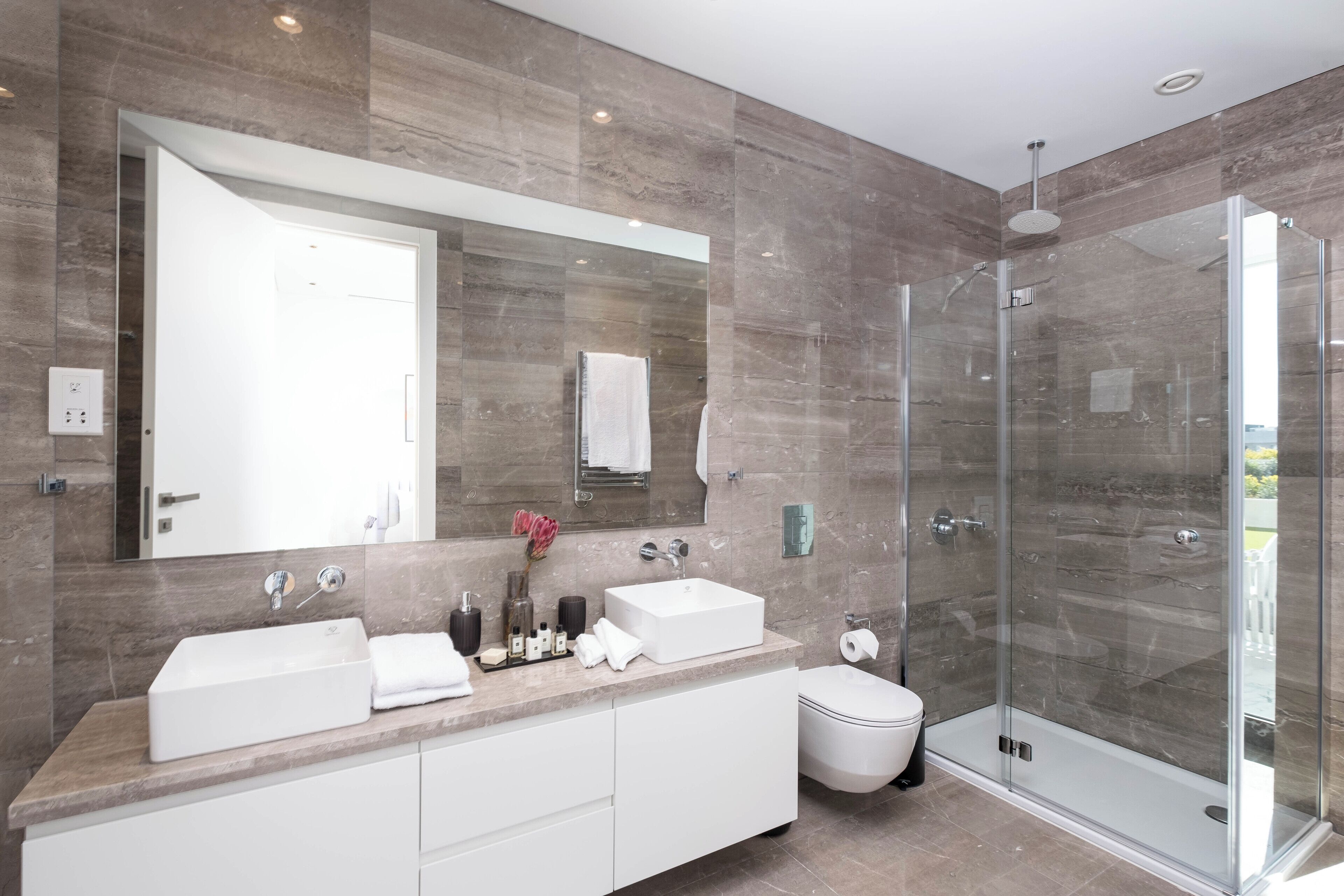 A modern bathroom with two sinks, a large mirror, a glass shower enclosure, and a toilet.